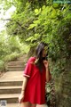 A woman in a red dress standing next to a stone wall.