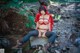 A woman in a red riding hoodie sitting on a rock in the woods.