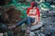 A woman in a red hooded outfit sitting on a rock in the woods.