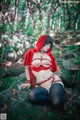 A woman in a red hooded outfit sitting on a rock in the woods.