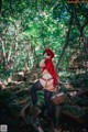 A woman in a red hooded outfit is posing in the woods.