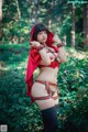 A woman in a red hooded outfit posing in the woods.