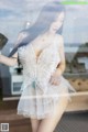 A woman in a white lingerie posing by a window.