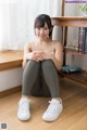 A woman sitting on the floor in front of a book shelf.