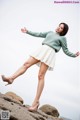 A woman in a green sweater and white skirt standing on a rock.