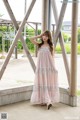 A woman in a pink dress standing in front of a wooden structure.