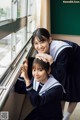 Two young women in school uniforms leaning against a window.